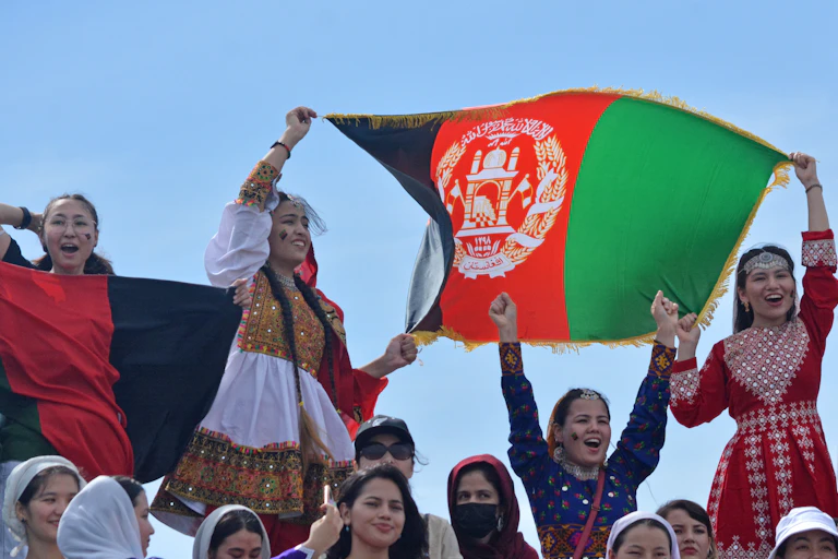 Women cheer and wave the Afghanistan flag during a cricket game in 2023
