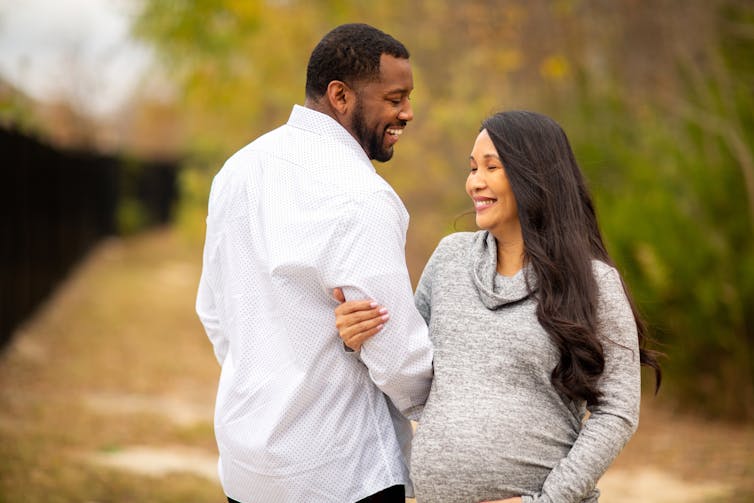 A couple outdoors smiling. The woman is pregnant.