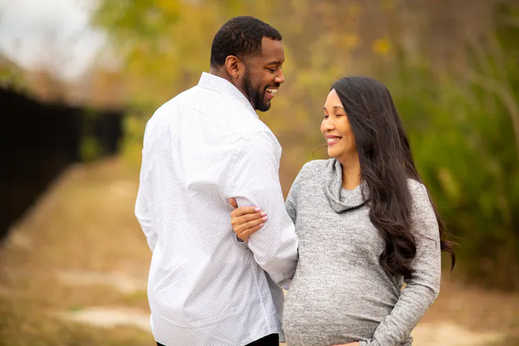 A couple outdoors smiling. The woman is pregnant.