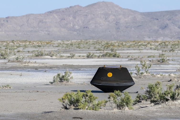 A black capsule sitting in the middle of the desert.