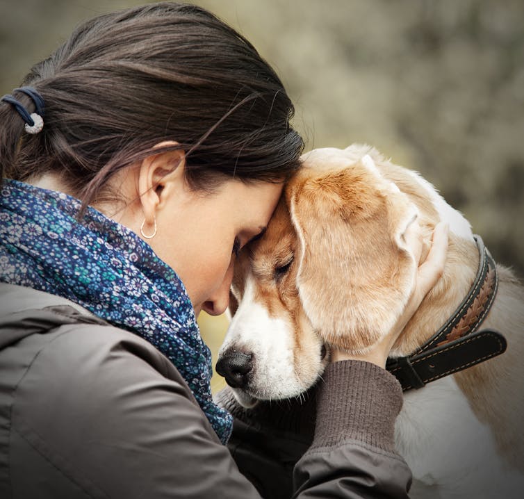 A woman presses her forehead lovingly against her dog's forehead.