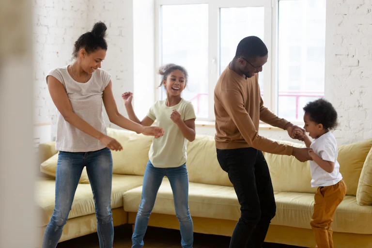A woman, man and two young children dance next to a couch.