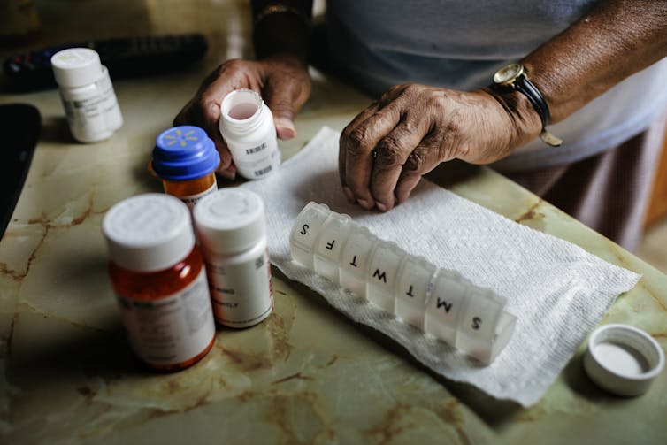 Person sorting through pills, a variety of pill bottles and a weekly pill box beside them