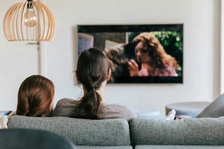 Two people sit on a couch, watching TV.