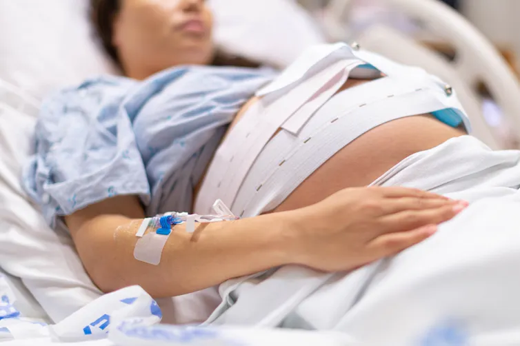 Pregnant woman lying in hospital bed wearing monitoring device around belly
