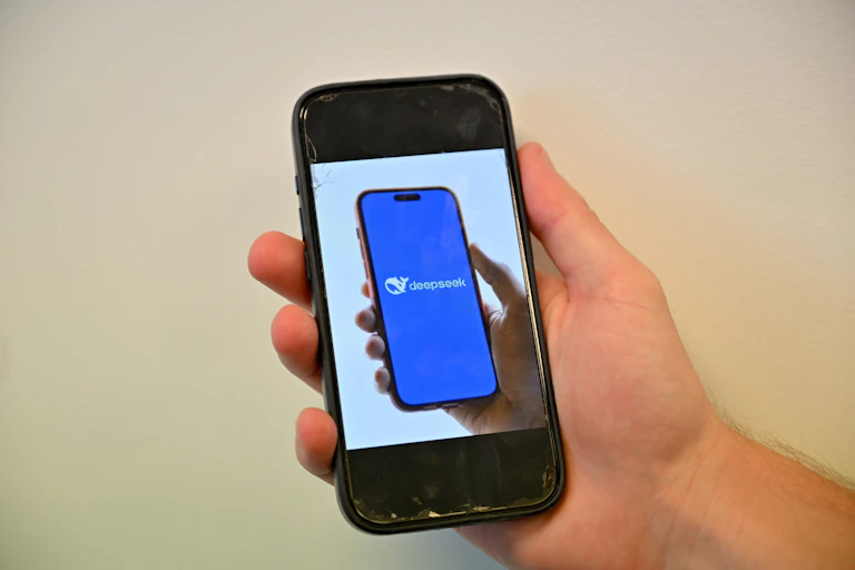 Photo of a person's hand holding a phone showing a photo of a person's hand holding a phone showing a stylised whale logo and the world "DeepSeek"