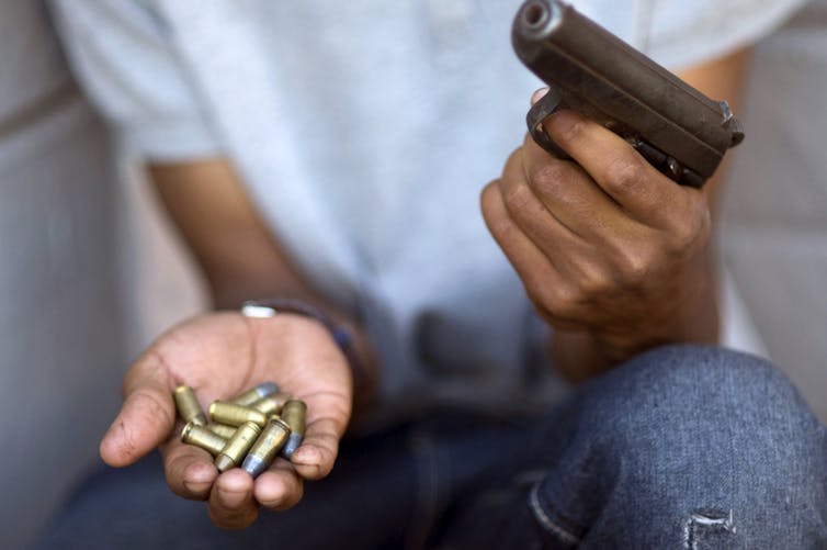 A man holds a gun in his left hand and several bullets in his right hand.