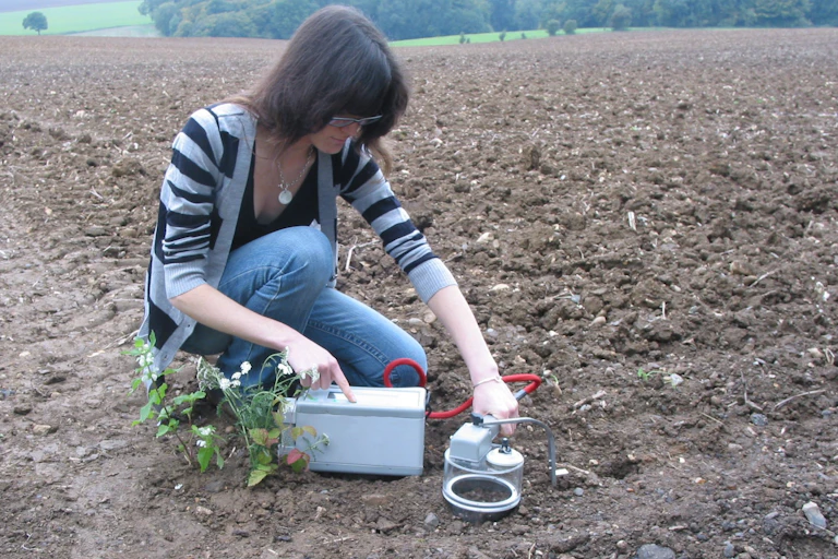 Woman kneeling down in a large field, holding a device against the ground.