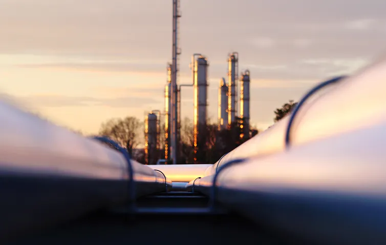 Close up of pipes heading towards an oil refinery in background.
