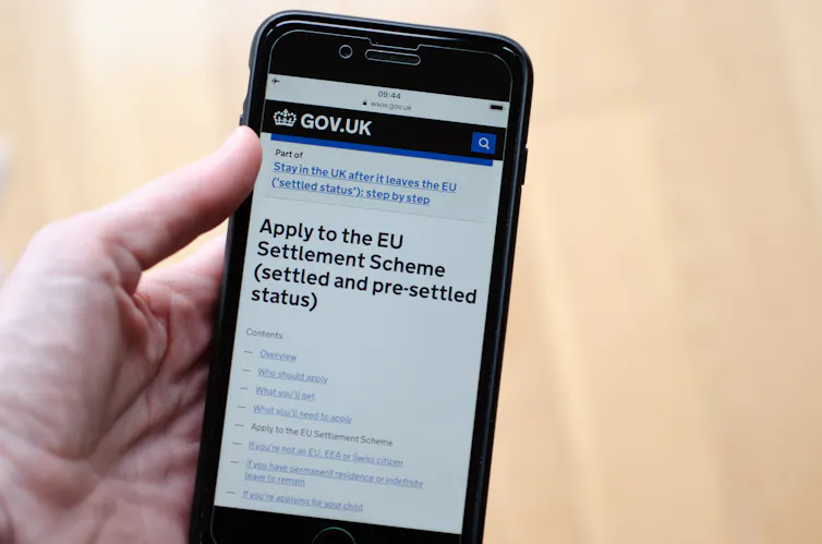 A hand holding a mobile phone that has the government application page for the EU settlement scheme pulled up