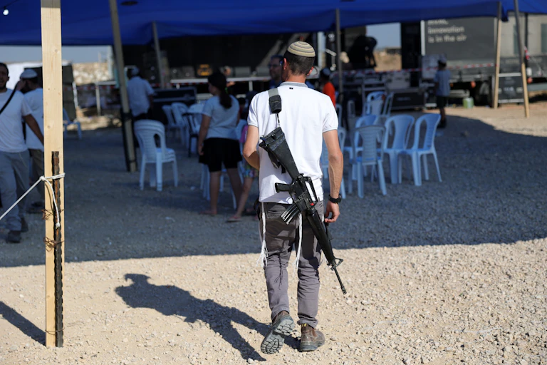 A young Israeli settler armed with a rifle at an open-air event near Gaza, October 2024.