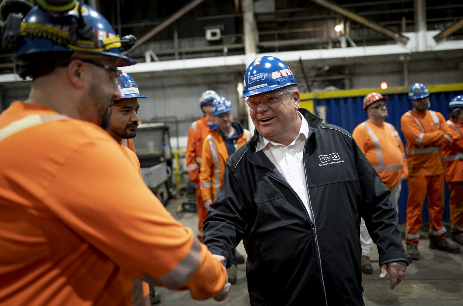 un homme portant un casque de protection serre la main d'un homme vêtu d'une combinaison orange et d'un casque de protection dans une usine