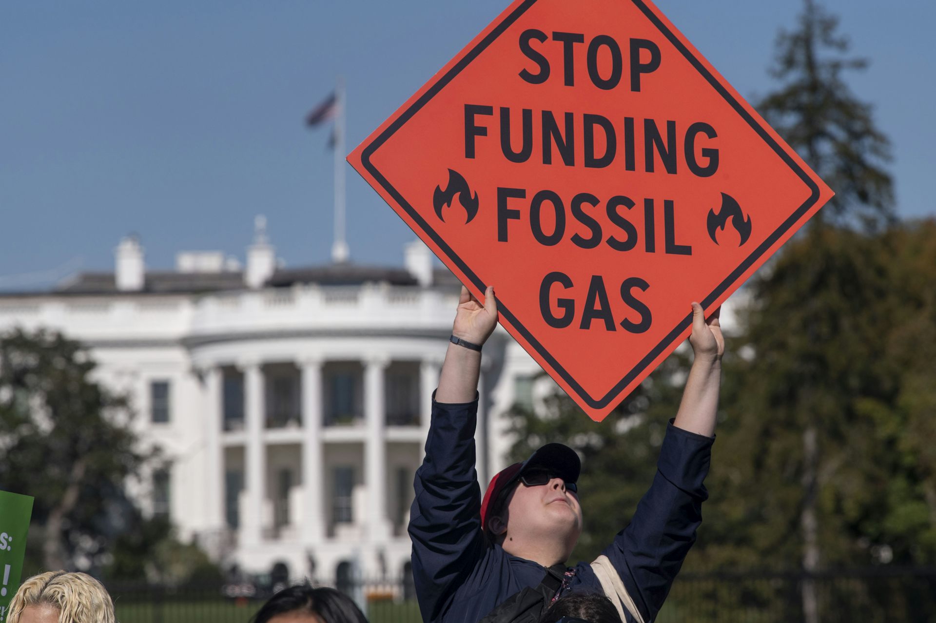 A protester carries an orange sign that reads Stop Funding Fossil Gas in front of the White House.