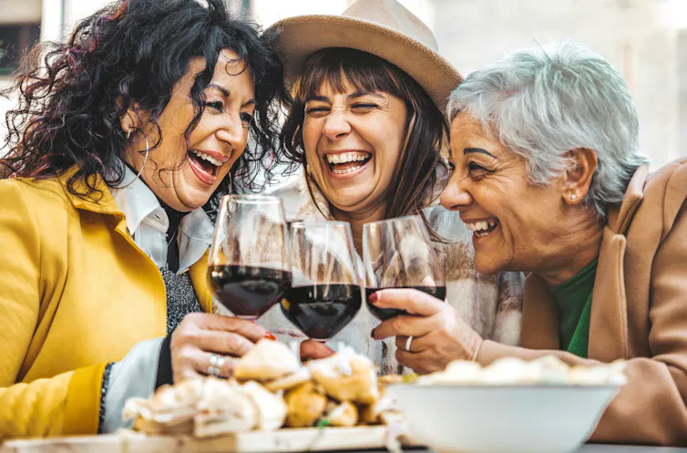 Three middle-aged women smiling and drinking red wine outdoors