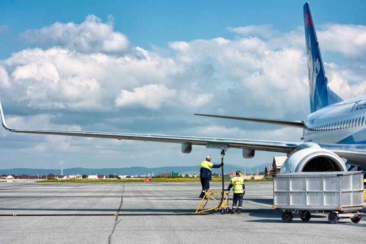 Technicians refuel an aeroplane on the runway.