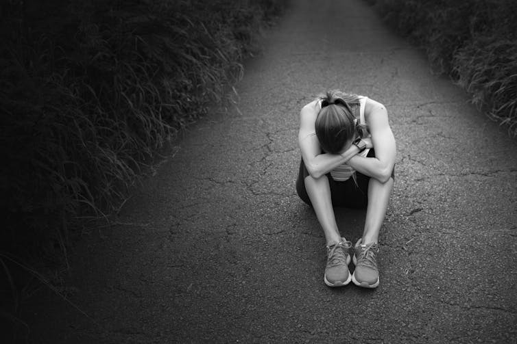 A girl sits on a road with her head down, resting on her bent knees.