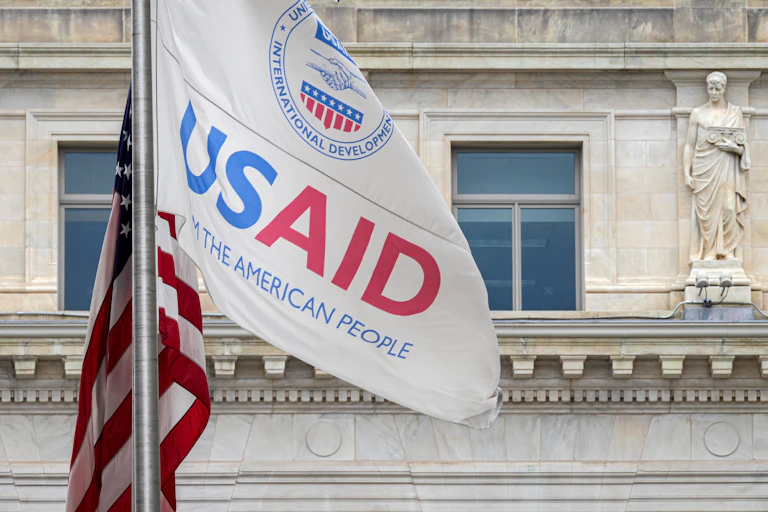 The USAID flag flies alongside the American flag outside an old building.