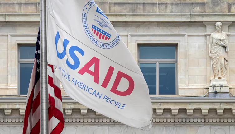 The USAID flag flies alongside the American flag outside an old building.