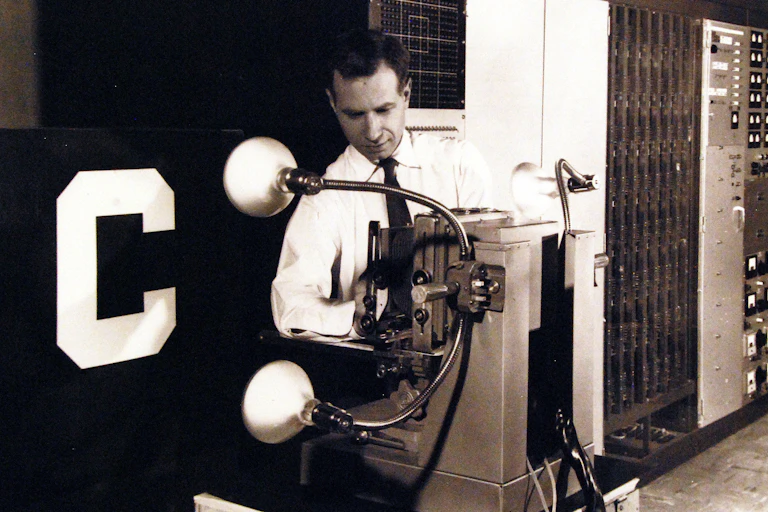 Black and white photograph of a man adjusting a complex machine