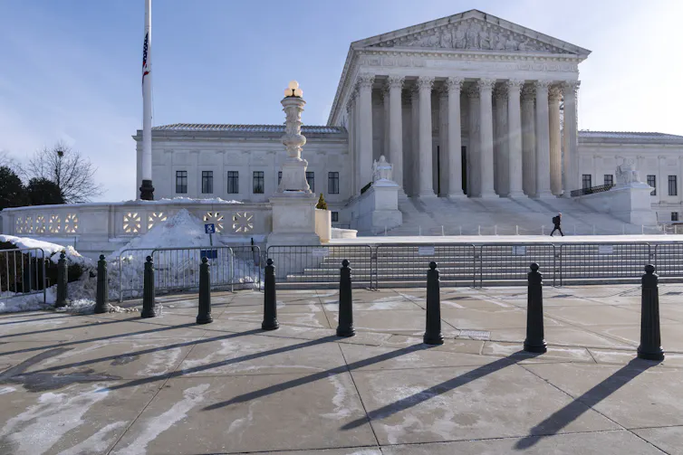 A large white building with tall columns sits atop tiers of steps, with a bit of snow in the foreground.