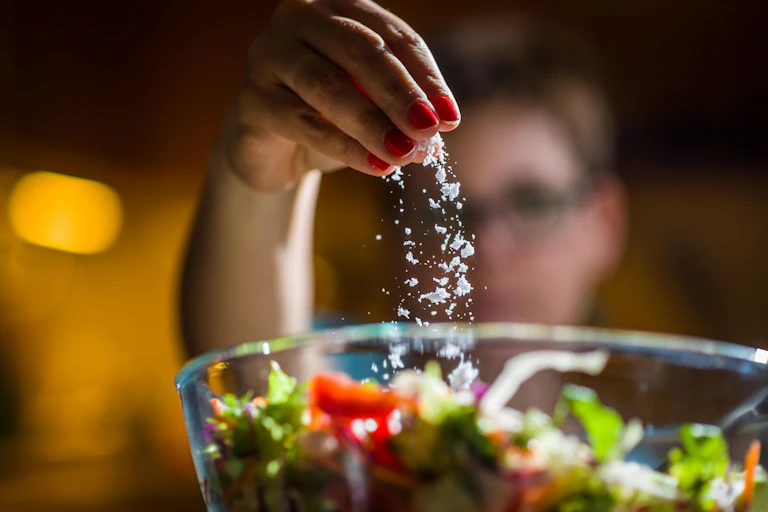 A woman sprinkling salt on salad.