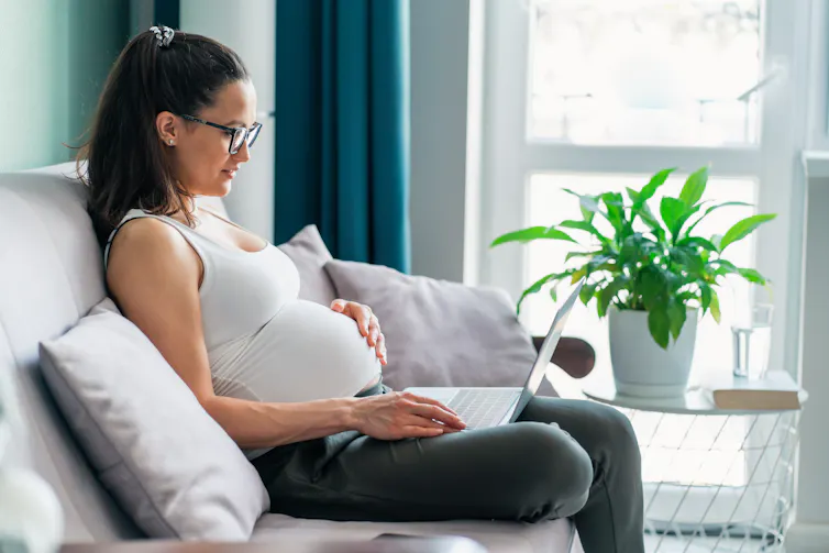 A pregnant woman sitting on a couch using a laptop.