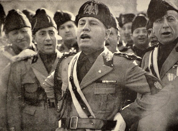 Italian dictator Benito Mussolini in uniform singing in a crowd of his soldiers.