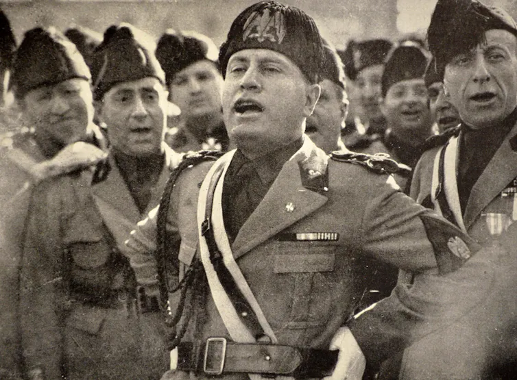 Italian dictator Benito Mussolini in uniform singing in a crowd of his soldiers.