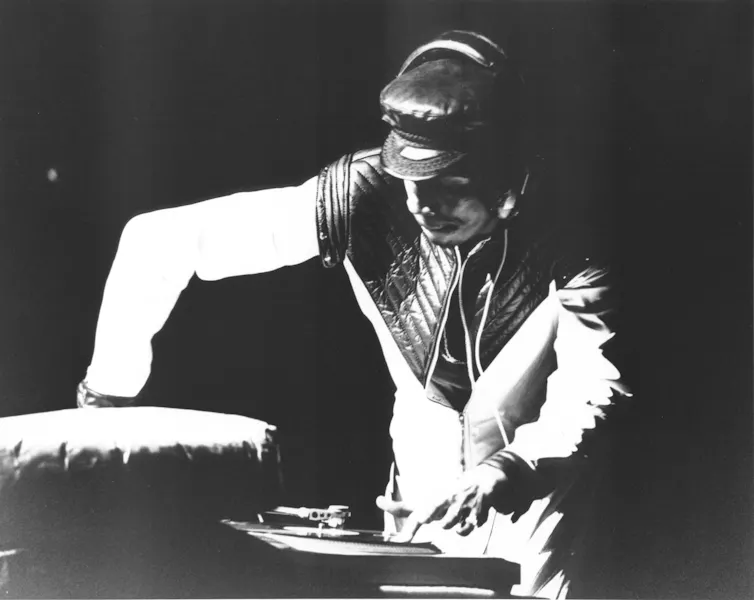 A man in headphones stands above a shooting style.
