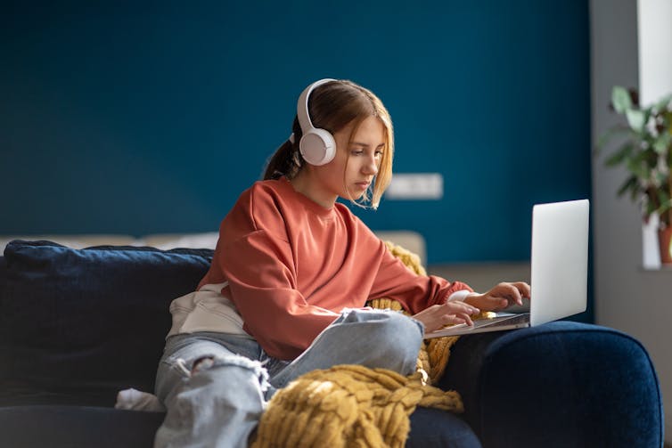 Teenage girl sat on sofa with headphones and laptop