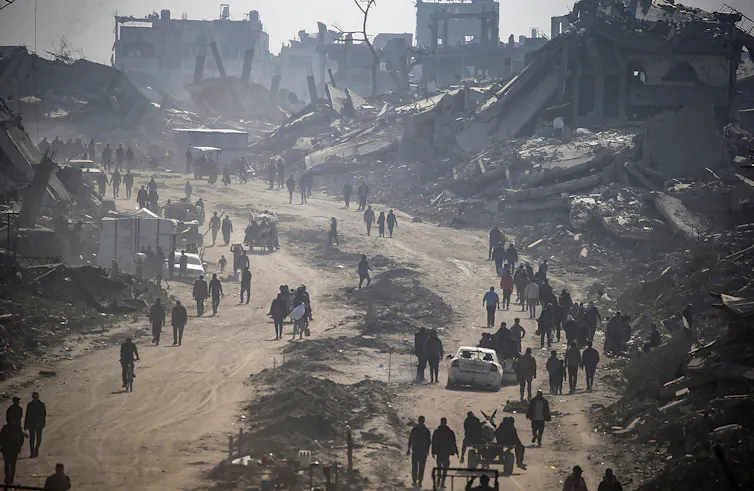 Palestinians walk among the rubble of destroyed buildings.