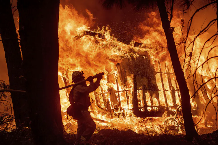 A fireman walks in front of a house engulfed in flames.