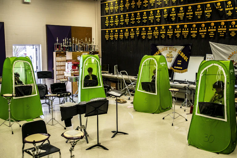 Four green pop up tents are arranged in a classroom with students seated inside them.