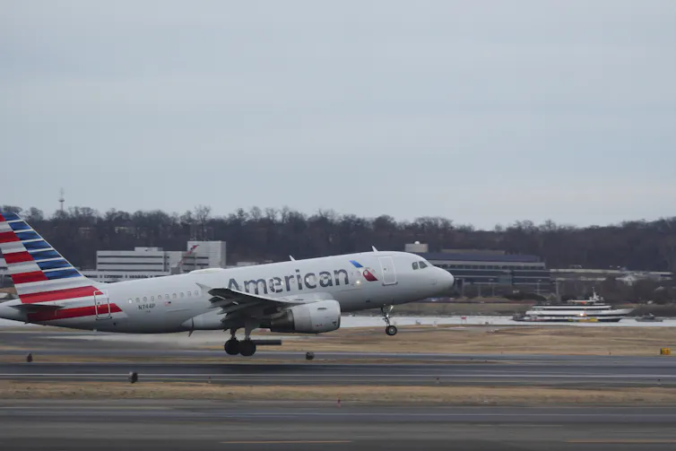 Aeroplane with an red stripes and blue stars on its tail landing on a runway.