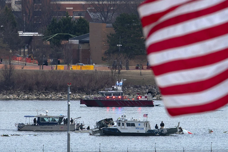 Boats and parts of a wreckage in still water, with an American flag fluttering in the foreground.