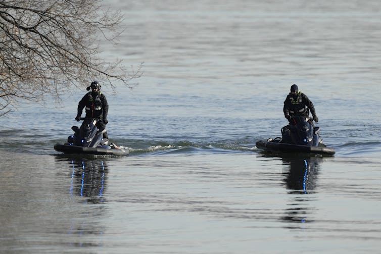 Two police officers scanning still water on jet skis.