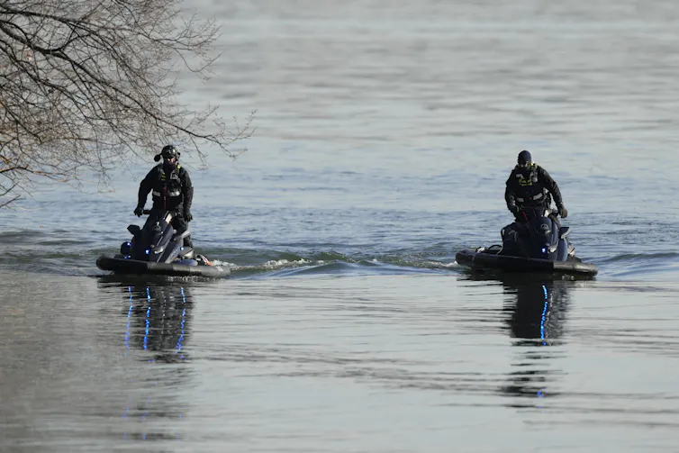 Two police officers scanning still water on jet skis.