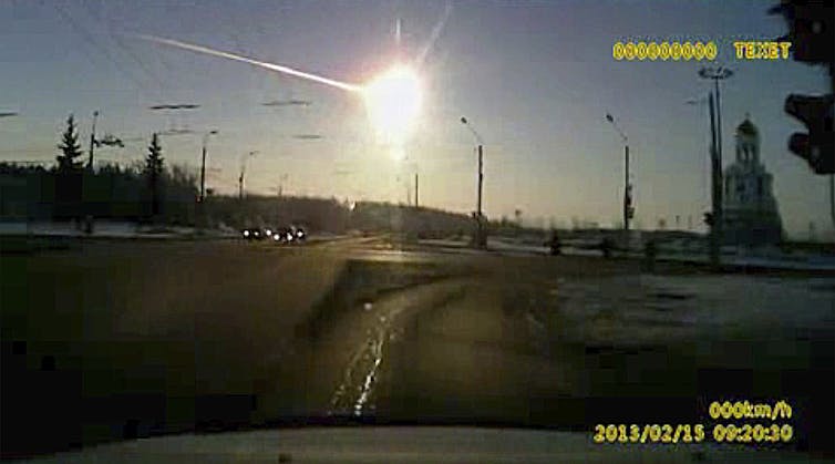 Photo from a dashboard camera showing a bright fireball streaking across the sky above a city
