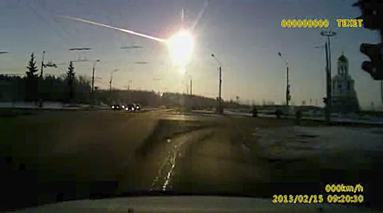 Photo from a dashboard camera showing a bright fireball streaking across the sky above a city