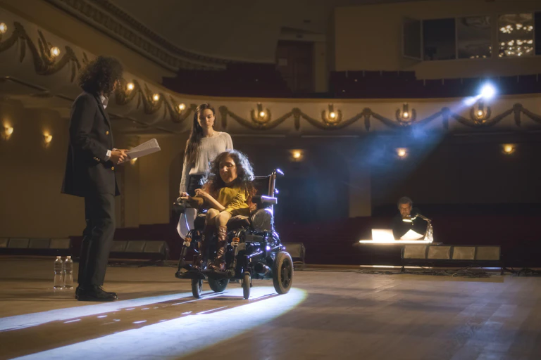 A woman actor in a wheelchair with two other actors on stage.