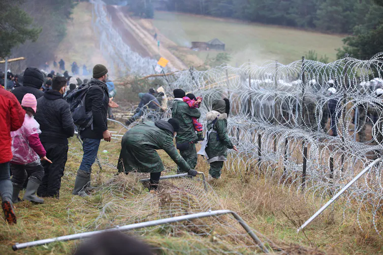 Men and women stand by a roll of barbed-wire.