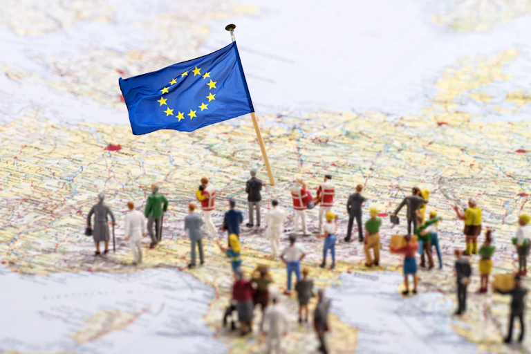 miniature models of people on a map of Europe with a European flag stuck in it.