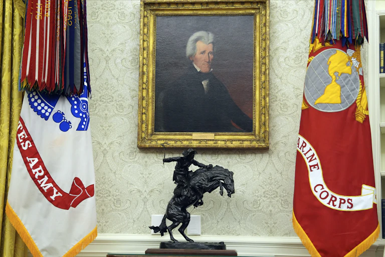 A painting of an old-looking man with gray hair, on a wall between two colorful flags.