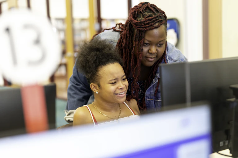Woman stands over girl's shoulder as they both look at computer monitor