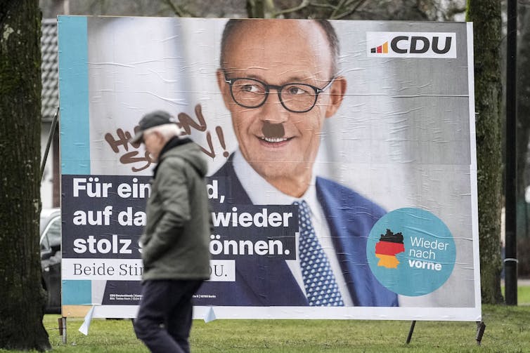 Defaced election poster showing Friedrich Merz with a Hitler moustache.