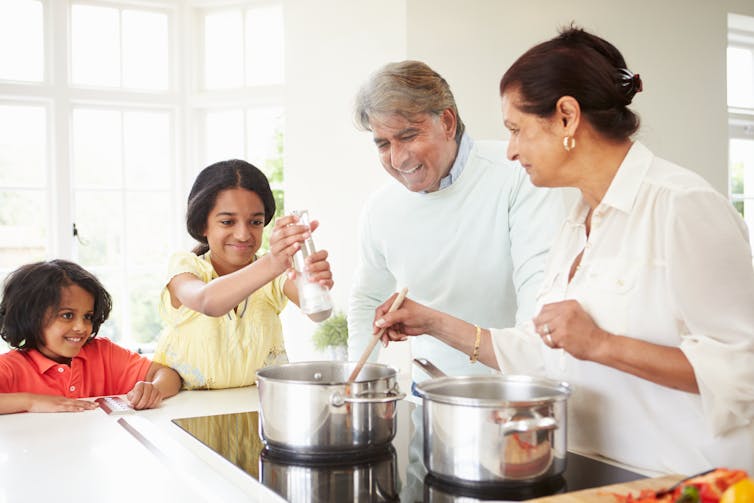 Two elderly adults cooking in a kitchen with two young children