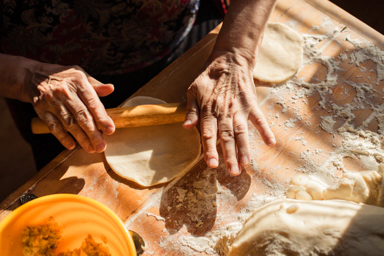 An older person's hands using a rolling pin to roll out some dough