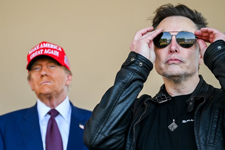 Two men together, one in a red baseball hat and the other wearing dark sunglasses.