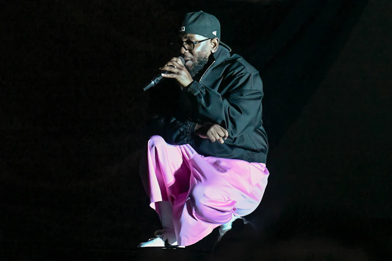 Man wearing backwards hat kneels on one knee while speaking into a microphone.