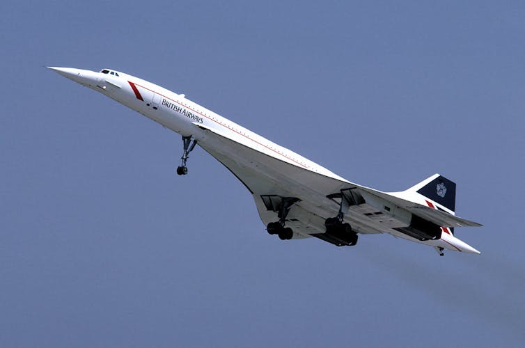 A long-nosed plane with short wings flies across a blue sky.